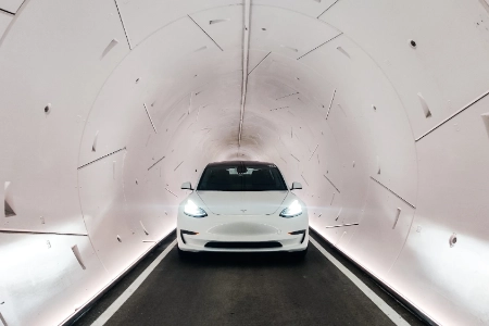 white tesla model y driving through futuristic underground tunnel in las vegas part of boring company loop transit system