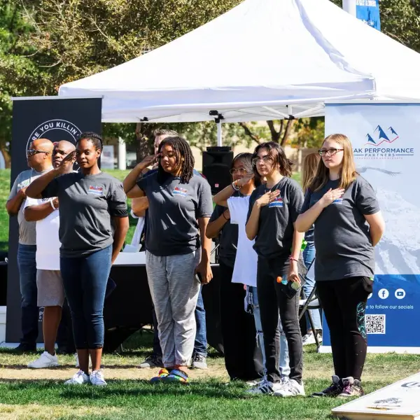 group of people with hands over hearts at vetfest in downtown summerlin las vegas with tents banners and cornhole game
