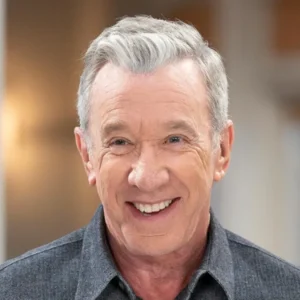 Smiling portrait of Tim Allen in a dark collared shirt with warm indoor lighting and soft background