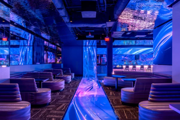 Futuristic lounge interior at Atomic Golf Las Vegas with blue and purple lighting curved booths and illuminated walkway