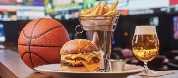 Cheeseburger, fries, and beer at The Tavern during March Mania at Fontainebleau Las Vegas with sports screens in the background