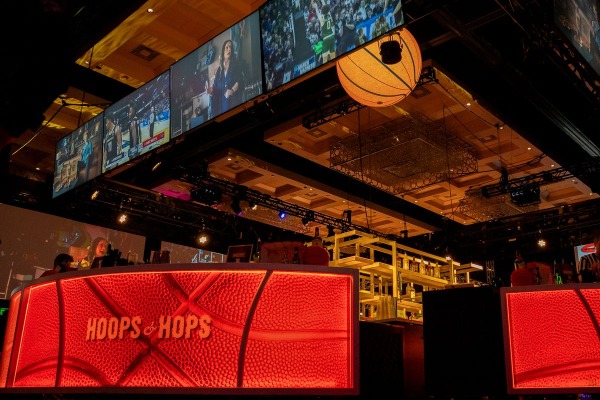 Basketball‑themed sports bar setup for Hoops & Hops at The Cosmopolitan of Las Vegas with large screens and a basketball‑textured bar