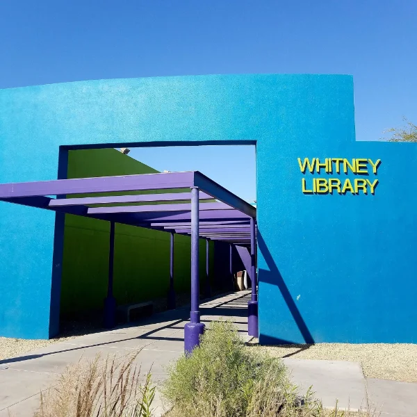 The vibrant blue and lime green exterior of Whitney Library in Las Vegas, featuring the purple shaded walkway entrance and yellow branch signage