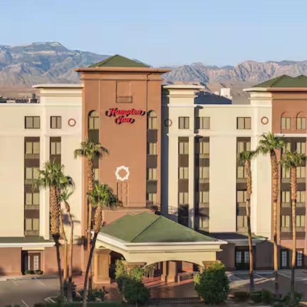 Exterior view of the Hampton Inn Tropicana in Las Vegas with palm trees, covered entrance, and mountain backdrop
