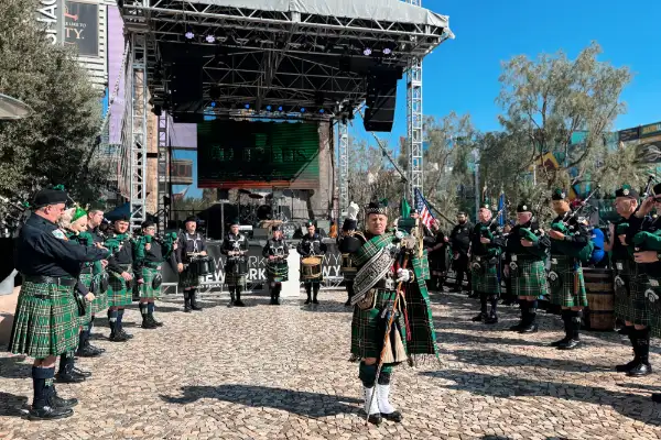 Celtic musicians in kilts performing with bagpipes and drums on an outdoor stage in Las Vegas with a large event screen and audience in the background