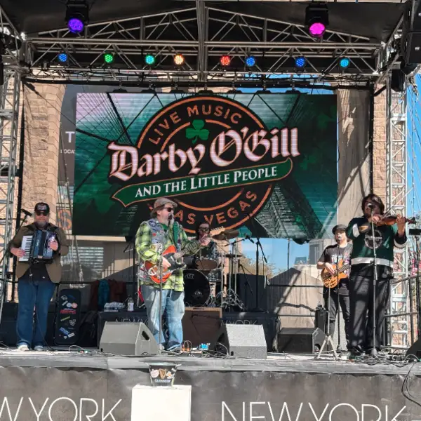 Darby O’Gill and the Little People performing live on an outdoor stage in Las Vegas with a digital screen displaying the band’s name and shamrock-themed graphics