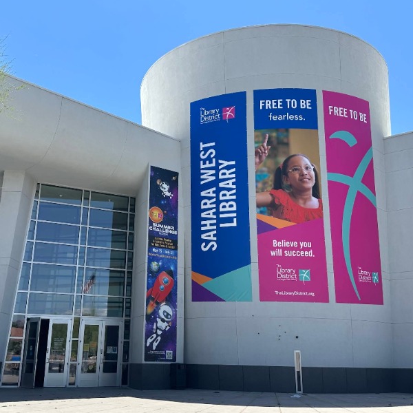 Exterior view of the West Sahara Library in Las Vegas featuring modern architecture, large banners, and the main entrance of the Las Vegas-Clark County Library District