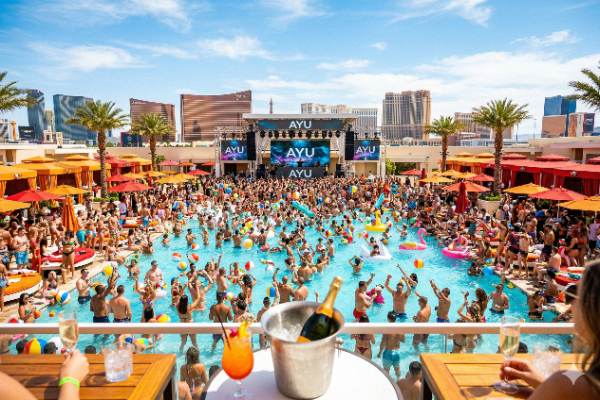 Crowded pool party at Ayu Dayclub in Resorts World Las Vegas, featuring a massive DJ stage against the city skyline.