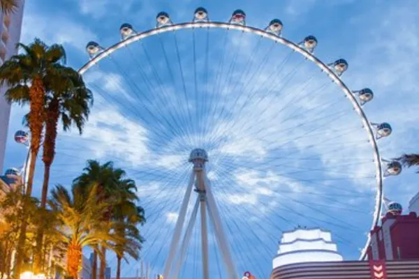 The High Roller at the LINQ Las Vegas glimmers in the sky on a sunny day with palm trees below.