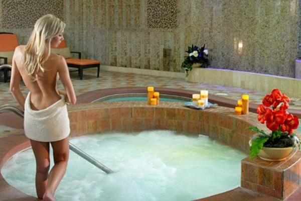 A woman wrapped in a towel stepping into a large circular hot tub whirlpool in the tiled wet area at Costa del Sur Spa inside the South Point Hotel Casino in Las Vegas