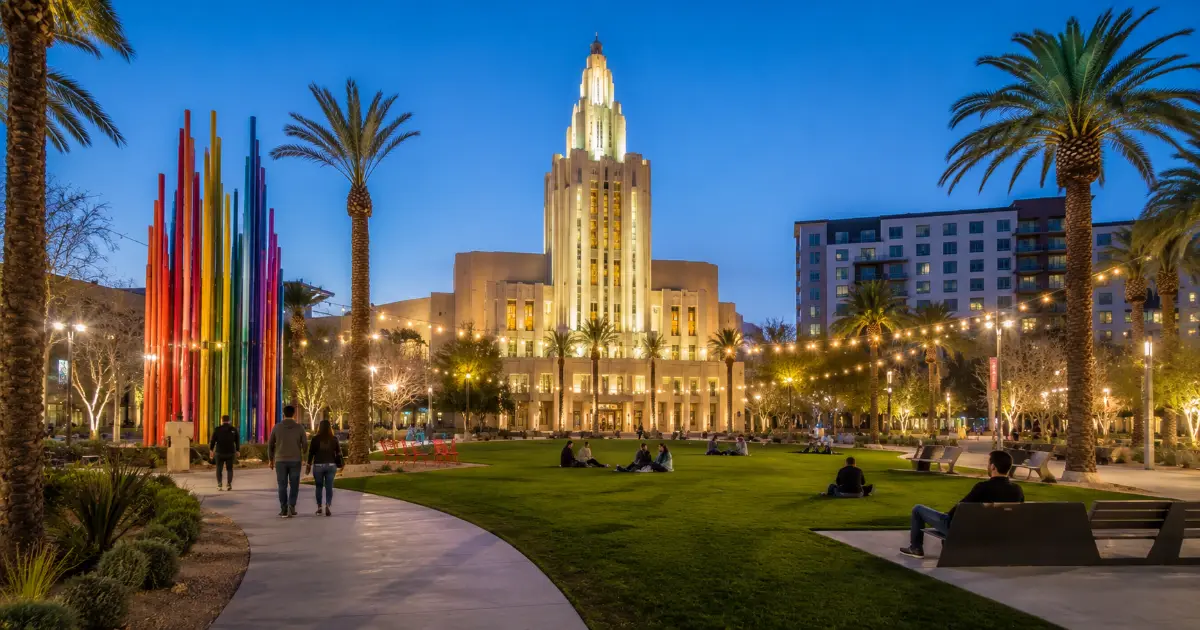 Evening view of Symphony Park in downtown Las Vegas featuring The Smith Center, landscaped lawns, public art, and visitors enjoying the outdoor gathering space.