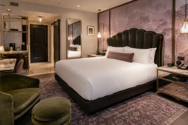 A guest room at The Vanderpump Hotel features tailored bedding, green seating, mirrored furnishings, and soft lilac accents.