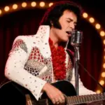 Rhinestone-jumpsuit tribute performer sings into a vintage microphone during All Shook Up Tribute to the King.