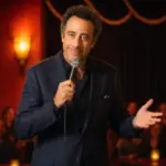 Brad Garrett smiles with a microphone beneath warm stage lights at his Las Vegas comedy club.