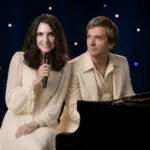 Carpenters Legacy performers Sally Olson and Ned Mills pose together beside a black grand piano.