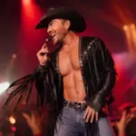 Chase Brown smiles onstage in a black cowboy hat and fringed leather jacket.