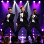 Three Chippendales performers dance in black tuxedos beneath purple and white spotlights.