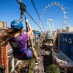 A rider soars above the LINQ Promenade on the Fly LINQ Zipline with the High Roller observation wheel in the background.
