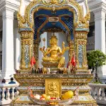 A close-up view of the golden Four-Faced Brahma statue housed in an ornate, tiled Erawan Shrine replica with vibrant gold and blue details, located outside Caesars Palace.