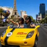 Couple explores the Las Vegas Strip in a yellow GoCar sightseeing vehicle while passing famous landmarks and resorts.