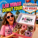 Smiling Las Vegas Donut Tour guide displays a colorful box of gourmet donuts near the Welcome to Fabulous Las Vegas sign.