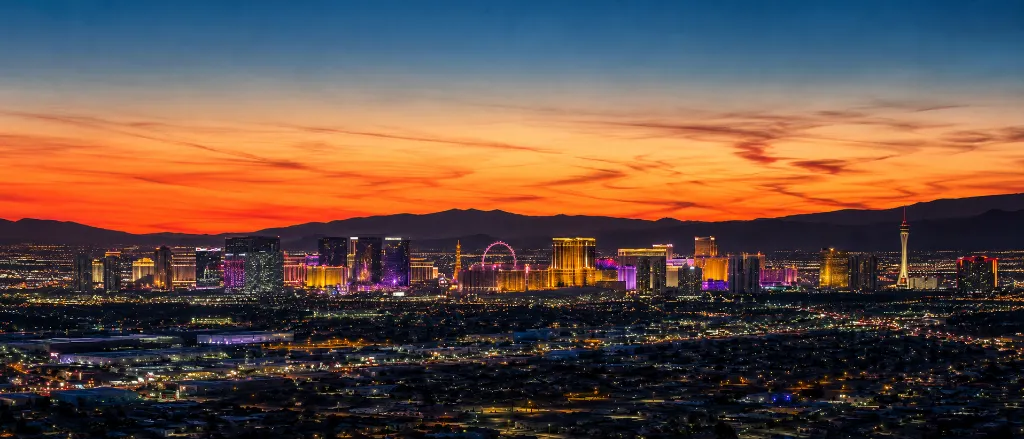 Panoramic view of the Las Vegas Strip and downtown skyline glowing beneath a vivid desert sunset and mountain backdrop.