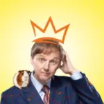 Mac King wearing a crown with a guinea pig on his left shoulder.