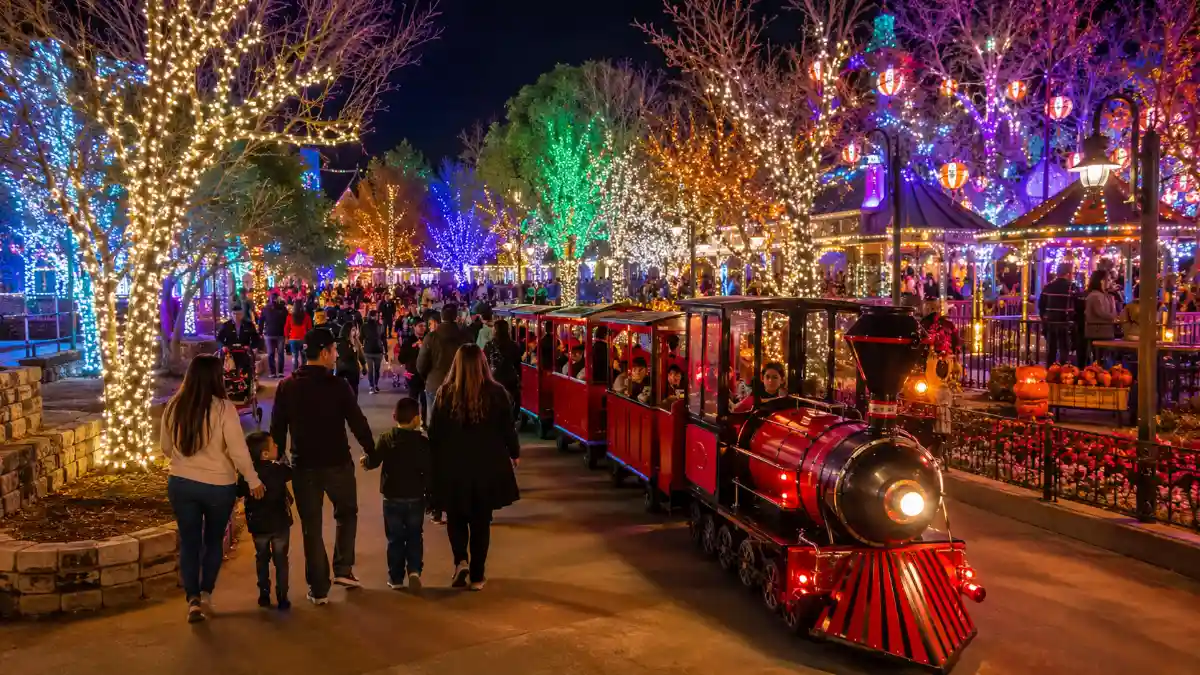Families stroll through the illuminated pathways and miniature train at Magical Forest at Opportunity Village in Las Vegas during a festive evening event.