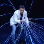 Magician Mat Franco performing in his show wearing a white coat with blue lightning shooting from his fingers.