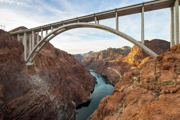 An upward view of the Mike O'callaghan Pat Tillman Memorial Bridge from a canyon floor and the Colorado River.