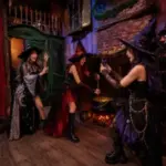 Three friends in witch cosplay laugh, stir a glowing cauldron, and take photos inside a spooky Las Vegas escape room.
