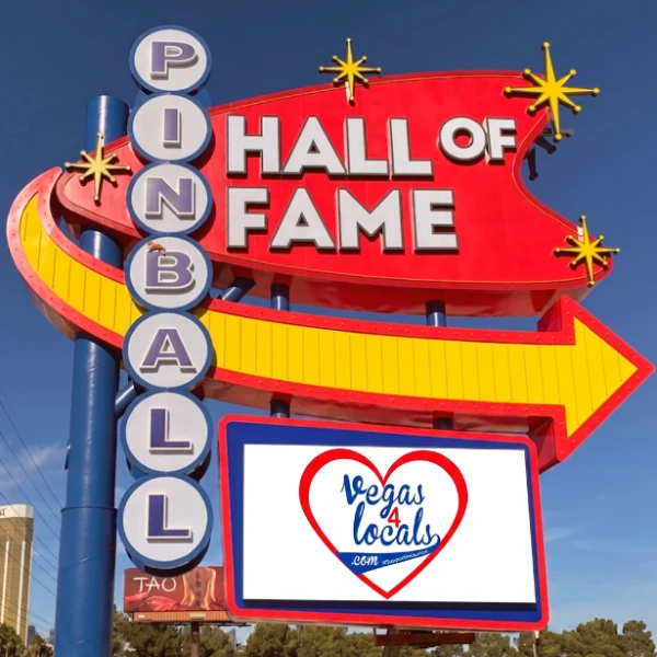 The iconic Pinball Hall of Fame neon sign in Las Vegas against a clear blue sky, featuring the red and blue Vegas4Locals.com heart logo centered on the illuminated lower display screen.
