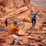 Hikers on a Red Rock Canyon Hiking Tour explore striking red rock formations while taking pictures of each other.