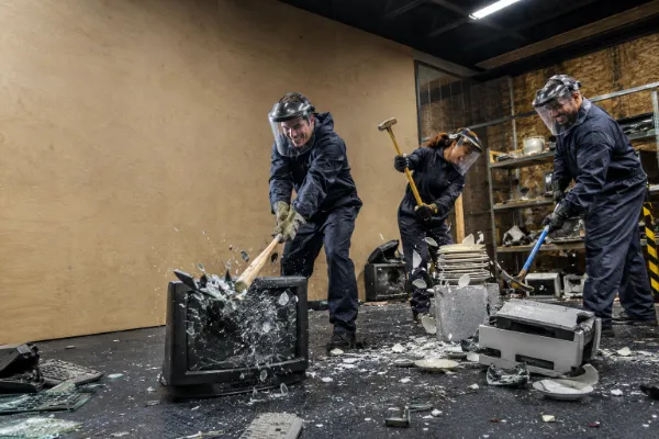 Three guests wearing protective safety gear smash electronics, glass, and household items during a Wreck Room Las Vegas rage room experience.
