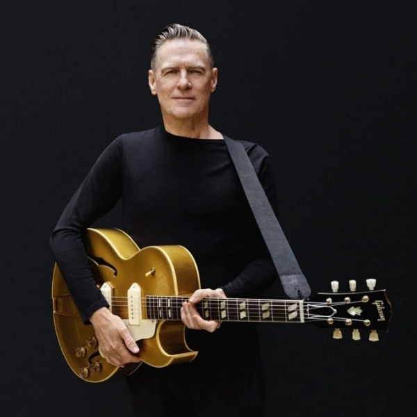 Bryan Adams holding a gold electric guitar in a promotional portrait for his Bare Bones acoustic concerts at Encore Theater.
