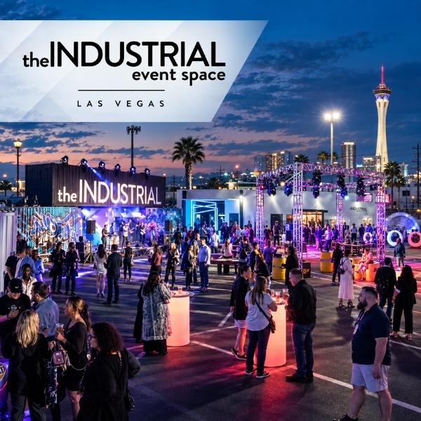 Guests mingle beneath colorful event lighting in the outdoor courtyard at The INDUSTRIAL Event Space, with the STRAT tower visible nearby.