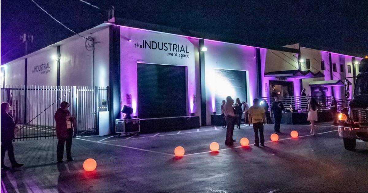 Guests mingle beneath colorful event lighting in the outdoor courtyard at The INDUSTRIAL Event Space, with the STRAT tower visible nearby.