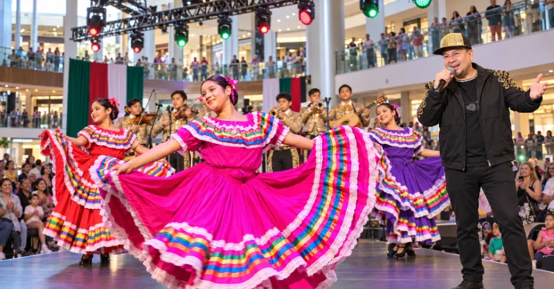 DJ Gabo hosts beside a folklórico dancer and youth mariachi musicians inside The Great Hall at Fashion Show Las Vegas.