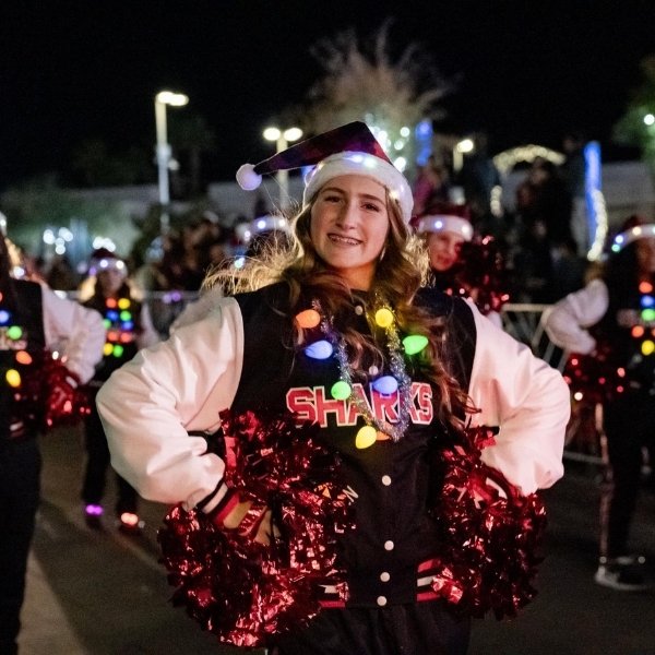 Cheerleader wearing a Santa hat and colorful holiday lights holds red pom-poms during Henderson WinterFest.