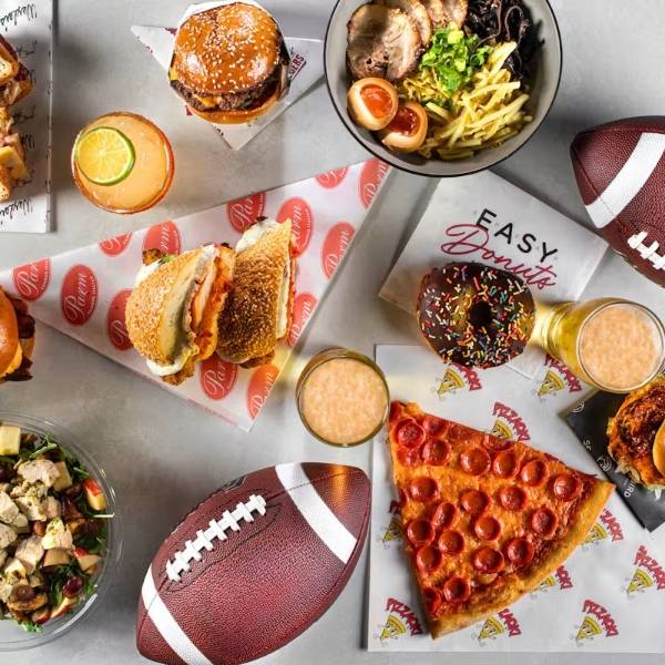 Burgers, pizza, sandwiches, fries, a doughnut and drinks arranged with footballs at Proper Eats Food Hall.