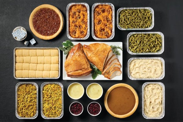 Cracker Barrel Thanksgiving Feast with two turkey breasts, sides, rolls, pumpkin pie and pecan pie arranged in serving trays.
