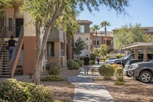 Residents walk through a modest, well-maintained Las Vegas apartment community with desert landscaping and covered parking.