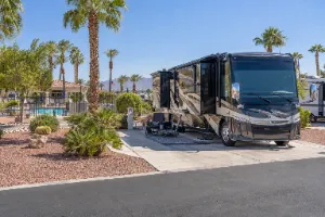 Class A motorhome at Desert Sands RV Park in Henderson with palm trees, a pool area, and desert landscaping