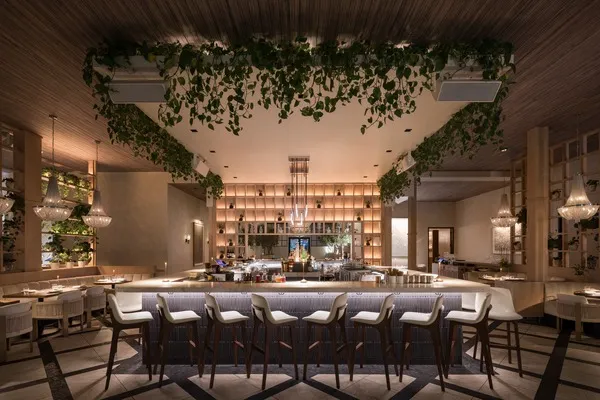 Guest House Las Vegas dining room with a central bar, upholstered stools, hanging greenery, and warm lighting.