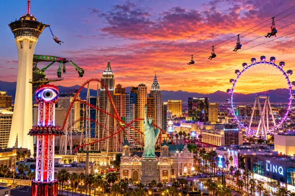 Las Vegas thrill rides at sunset, featuring The STRAT Tower, Eye Dropper, a looping roller coaster, ziplines, and the High Roller observation wheel.
